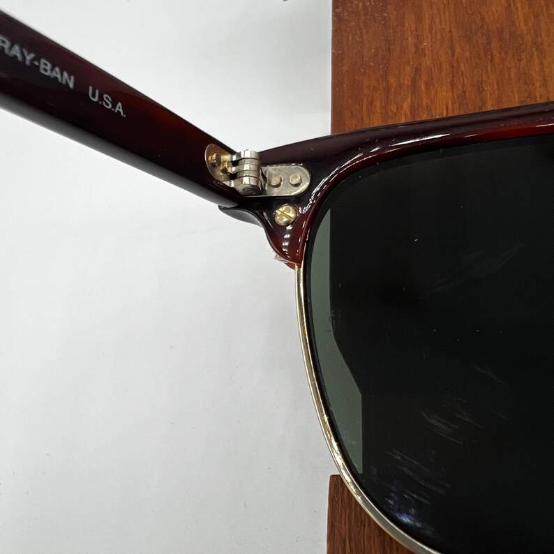 May include: Close-up of Ray-Ban sunglasses with a dark brown frame and black lenses. The hinge is silver, and the arm is marked "RAY-BAN U.S.A." The sunglasses have a classic design.