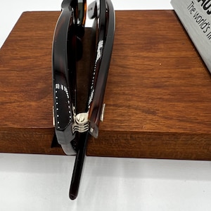 Puede incluir: Una pinza para el pelo grande, de carey, con cierre met&aacute;lico. La pinza es de color marr&oacute;n oscuro con veteado marr&oacute;n claro y est&aacute; apoyada sobre una superficie de madera. La pinza est&aacute; dise&ntilde;ada para sujetar una gran cantidad de cabello.