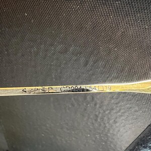 Pu&ograve; includere: Primo piano di un cucchiaio d'argento con segni. Il cucchiaio ha una superficie lucida e riflettente. Il testo sul cucchiaio include i numeri "C2004 54 19". Il cucchiaio &egrave; posto su uno sfondo scuro.