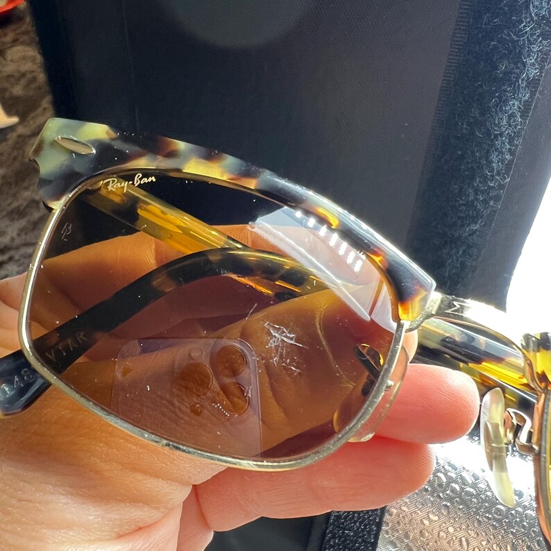 May include: Ray-Ban sunglasses with a tortoiseshell frame and brown lenses. The sunglasses have a classic design with a metal bridge and arms. The lenses have some scratches. The Ray-Ban logo is visible on the top left lens.