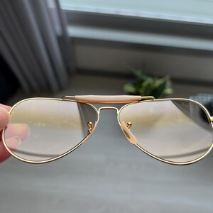 May include: Gold aviator sunglasses with brown lenses. The sunglasses have a brown bridge and gold metal frames.