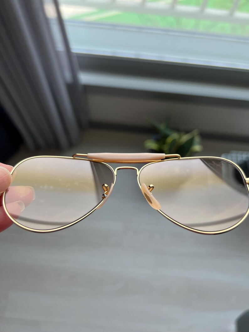 May include: Gold aviator sunglasses with brown lenses. The sunglasses have a brown bridge and gold metal frames.