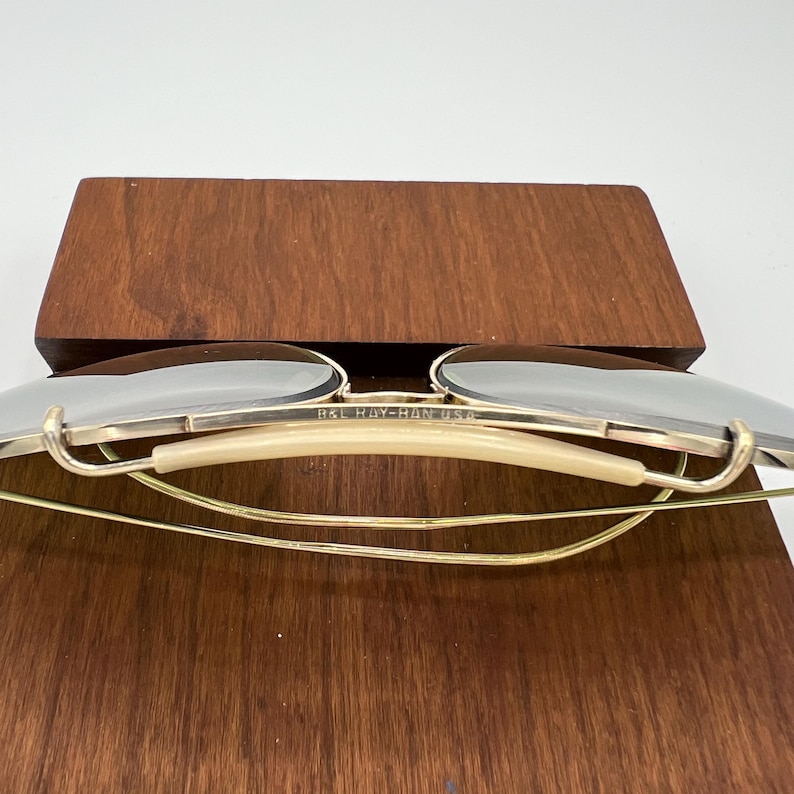 K&ouml;nnte beinhalten: Goldfarbene Ray-Ban USA Aviator-Sonnenbrille mit cremefarbenem Nasensteg und verspiegelten Gl&auml;sern.