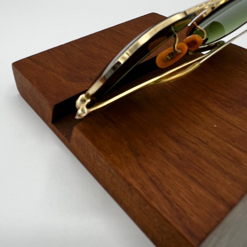 May include: A wooden wine bottle holder with a gold-colored metal frame. The holder is designed to cradle a wine bottle, with a slot in the wooden base. The frame has decorative elements and holds the bottle at an angle.