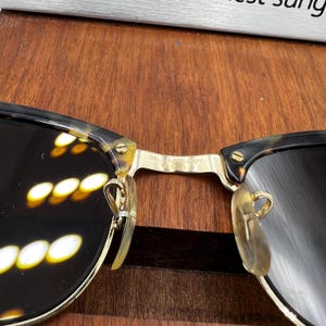 May include: Close-up of vintage sunglasses with a tortoiseshell pattern on the frames. The lenses are dark, and the metal bridge features the text "B&L RAY-BAN". The sunglasses have a classic, retro design.