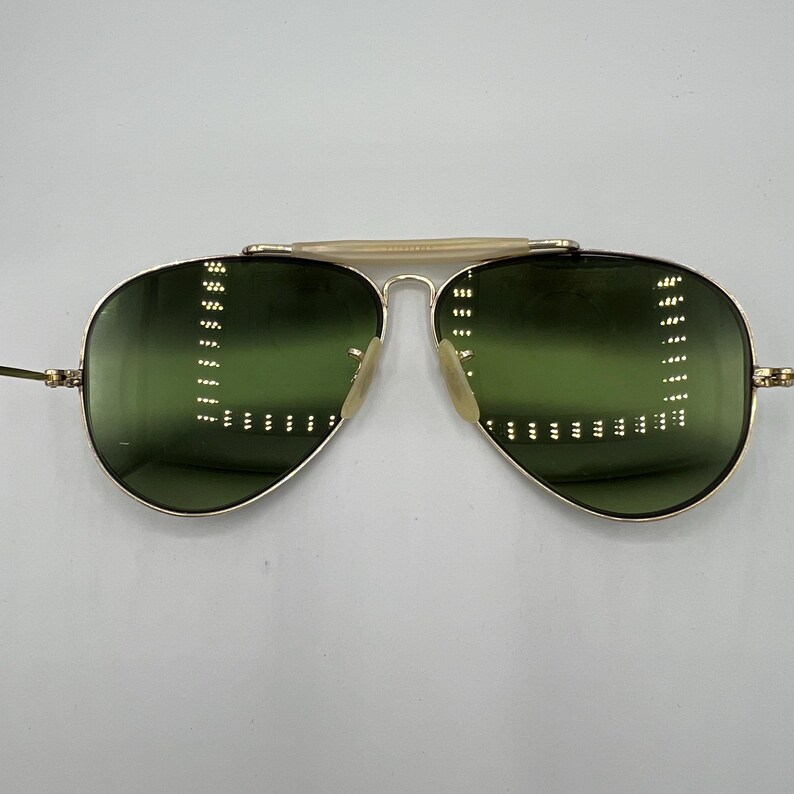 K&ouml;nnte beinhalten: Goldene Aviator-Sonnenbrille mit gr&uuml;nen Gl&auml;sern. Die Sonnenbrille hat einen d&uuml;nnen goldenen Metallrahmen und eine goldene Metallbr&uuml;cke.