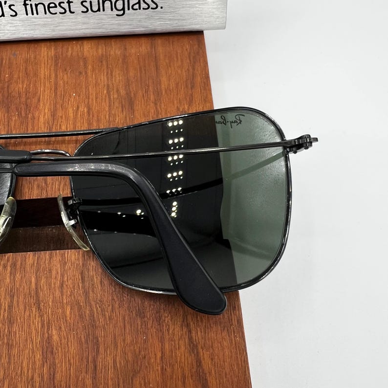 K&ouml;nnte beinhalten: Schwarze Sonnenbrille mit Metallrahmen und dunklen Gl&auml;sern. Die Sonnenbrille hat einen klassischen Aviator-Stil mit Doppelsteg und einem schlanken, modernen Design. Die Gl&auml;ser sind dunkelgr&uuml;n.