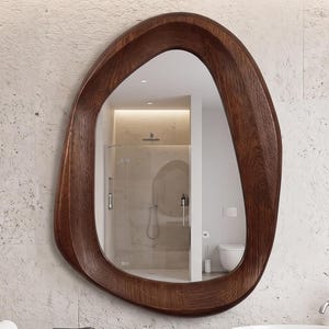 May include: A wall-mounted bathroom vanity featuring a dark wood finish with two drawers, a white ceramic vessel sink, and a chrome faucet. Above the vanity hangs an organic, asymmetrical mirror with a thick, dark wood frame reflecting a bathroom.