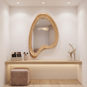 May include: A wall-mounted vanity area featuring a light wood floating shelf, a light wood organic-shaped mirror, a beige velvet ottoman, a makeup organizer with cosmetics, a brush holder, and a light-colored branch-style jewelry stand.