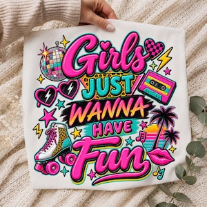 May include: A white t-shirt featuring a colorful graphic with the text Girls JUST WANNA HAVE FUN. The design includes a disco ball, heart-shaped sunglasses, a cassette tape, a leopard print roller skate, palm trees, and a pair of pink lips.