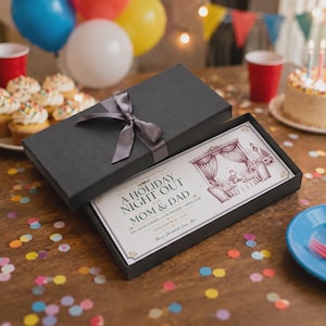 May include: A black rectangular gift box with a grey satin ribbon bow, containing a printed card titled A HOLIDAY NIGHT OUT FOR MOM & DAD. The card features a maroon line drawing of a dining room and text detailing a dinner, theater, and car service.