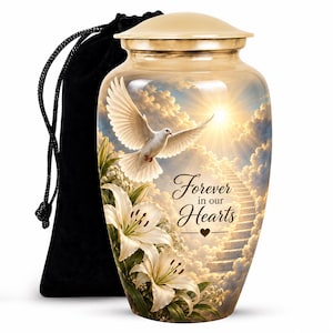 May include: A gold-toned metal cremation urn featuring a printed scene of a white dove flying toward a sunlit staircase in the clouds, with white lilies and the text Forever in our Hearts. A black velvet drawstring bag is positioned behind the urn.