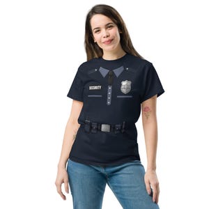 May include: A navy blue short-sleeve t-shirt featuring a printed security uniform design. The graphic includes a collar, a black tie, a silver badge, a button-down placket, and a utility belt with pouches. The word SECURITY is printed in white.