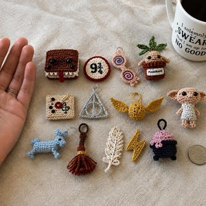 May include: A collection of small, crocheted items including a brown book with teeth, a red 9 3/4 sign, pink glasses, a potted mandrake, a beige map, a silver triangle symbol, a gold snitch, a small creature, a blue animal, a brown tassel, a white feather, a yellow lightning bolt, and a black cauldron.