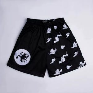 May include: Black athletic shorts featuring a split design. The left side displays a white circular patch with a black silhouette of a running figure. The right side is patterned with white stylized cloud shapes. The shorts have an elastic waistband.
