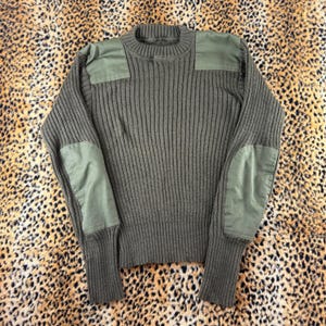 May include: An olive green ribbed knit sweater featuring matching fabric patches on the shoulders and elbows. The garment has a crew neckline, long sleeves with ribbed cuffs, and a thick, textured knit construction throughout the torso and sleeves.