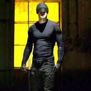 Puede incluir: Una figura con una camiseta negra de manga larga, pantalones tácticos negros con cinturón, guantes negros y un gorro negro. La figura sostiene un objeto cilíndrico largo, fino y de color claro en una mano frente a una ventana amarilla brillante.