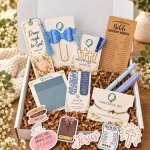 May include: A white gift box containing religious stationery items including a floral bookmark with the text Draw nigh to God, a blue bow paperclip, cross-shaped bookclips, a Bible emergency numbers card, stickers, a bracelet, and two pens.