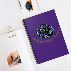 May include: A spiral-bound notebook with a deep purple cover featuring a coiled snake graphic in shades of blue, green, and black, with yellow eyes. The text "Bridgett Nelson Horror" is printed in gold lettering beneath the snake illustration.