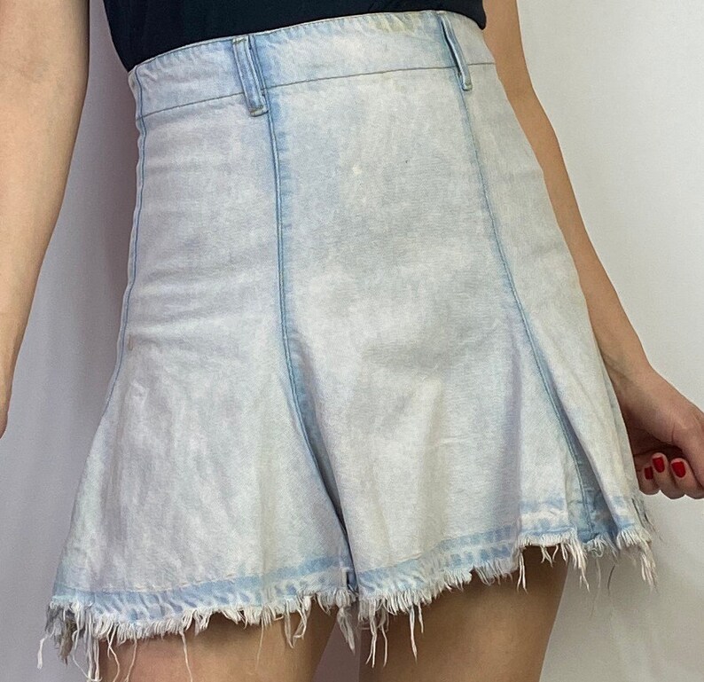 May include: A light blue denim skirt with a frayed hem. The skirt has a high waist and a slightly flared silhouette.