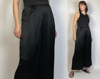 Peut inclure: Pantalon large en satin noir à taille haute et plis. Le pantalon est fluide et a une texture soyeuse.