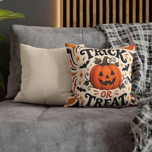 May include: A square throw pillow featuring a central orange jack-o'-lantern pumpkin graphic surrounded by black bats, orange stars, and swirling vines. The text "TRICK OR TREAT" is printed in a bold black decorative font above and below the pumpkin.