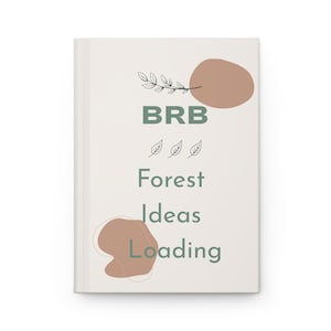 May include: A white hardback notebook featuring the text BRB Forest Ideas Loading in sage green. The cover includes two abstract tan organic shapes and a black line drawing of a leafy branch, along with three small black leaf icons centred.