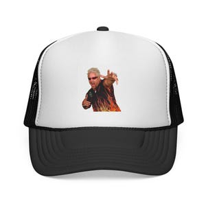 May include: A white and black trucker hat featuring a graphic print of a person with spiky blonde hair, sunglasses, and a black shirt with orange flame patterns. The cap has a solid white front panel, a black brim, and black mesh side panels.