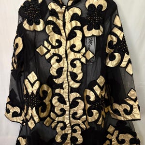 May include: A sheer black long-sleeve jacket featuring prominent gold metallic scrollwork appliqués and black beaded accents. The garment has a mandarin collar, a front button closure, and a structured pattern of gold fabric shapes throughout.