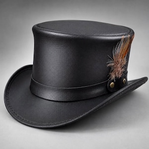 May include: A black top hat featuring a smooth finish, a wide brim, and a matching black leather-like band around the base. The band is secured with two small brass-colored metal studs and is accented with a cluster of brown and tan feathers.