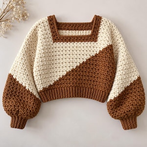 May include: A long-sleeve crochet jumper featuring a colour-blocked diagonal design in cream and brown. The garment has a square neckline, a cropped length, and ribbed cuffs at the wrists and hem, constructed with a textured stitch pattern throughout.