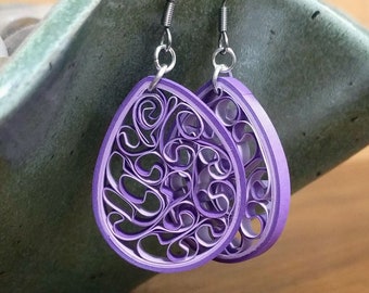 May include: A pair of purple paper quilling earrings with a delicate, intricate design. The earrings are made with thin strips of paper that are rolled and shaped into a floral pattern. The earrings are attached to silver hooks.
