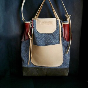 Könnte beinhalten: Eine blaue und weiße gemusterte Tragetasche mit einer braunen Lederklappe und einem roten Quasten. Die Tasche hat einen langen Riemen und einen kleineren Griff. Die Tasche trägt den Text "LOVE IS LOVE CO." auf der Vorderseite.