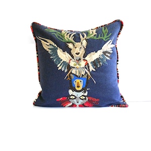 May include: A blue pillow with a red and black plaid trim features a totem pole design with a deer, owl, bear, and raccoon.