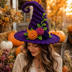 May include: A purple crocheted witch hat featuring a spiraled, pointed crown and a wide, scalloped brim. The hat is decorated with three handmade crocheted flowers in orange, pink, and dark purple, accented with green crocheted leaves and vines.