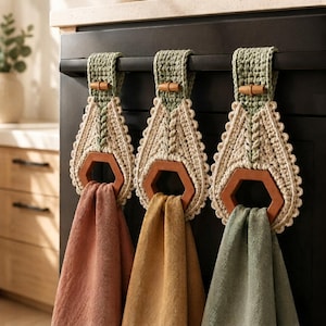 Peut inclure: Trois porte-serviettes en crochet avec des boucles de suspension vert sauge munies de petits boutons en bois, des parties supérieures en crochet texturé crème et des anneaux hexagonaux en bois. Chaque anneau retient une serviette en terre cuite, moutarde et vert sauge.