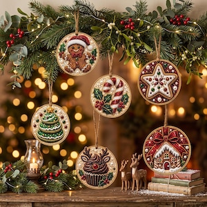 May include: Six round Christmas ornaments featuring diamond art designs: a gingerbread person, a candy cane with holly, a star, a Christmas tree, a reindeer cupcake, and a gingerbread house with a red bow, all hanging from jute twine strings.