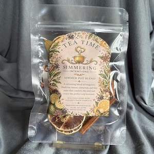 May include: A clear plastic pouch containing a simmer pot blend of dried botanicals, including cinnamon sticks and dried citrus slices. The label features the text Tea Time Simmering Intentions Simmer Pot Blend, listing ingredients like bergamot, black tea, lemon, cinnamon, and star anise.