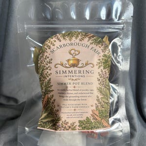May include: A clear plastic pouch containing a simmer pot blend labeled Scarborough Fair Simmering Intentions. The label features botanical illustrations of herbs and text describing an earthy blend of parsley, sage, rosemary, thyme, and cedarwood.