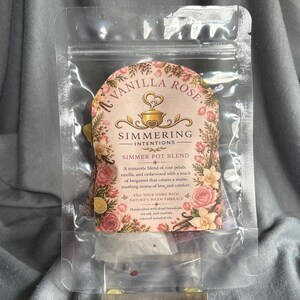 May include: A clear plastic resealable pouch containing a Vanilla Rose Simmering Intentions simmer pot blend. The label features floral illustrations, a pot icon, and text describing a blend of rose petals, vanilla, cedarwood, and bergamot.