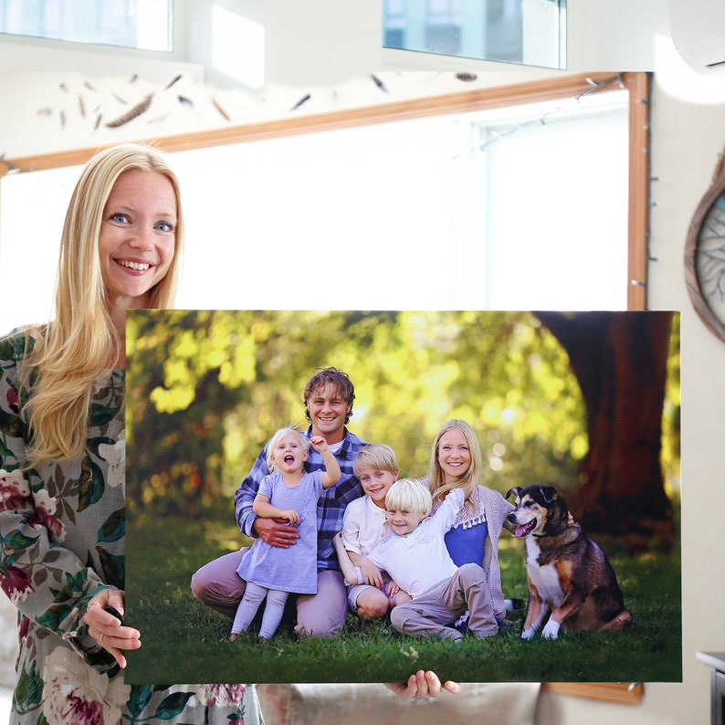 Op de afbeelding: Een familieportret afgedrukt op canvas, met een stel met drie kinderen en een hond. De familie poseert in een parksetting met groen gras en bomen op de achtergrond. De foto is in warme kleuren met een zachte focus.