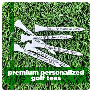 May include: A set of six white golf tees with black text that reads "Justin Michelle 2024" on each tee. The tees are arranged on a green grassy surface.  premium personalized golf tees