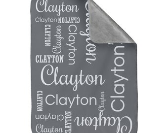 May include: Gray baby blanket with the name Clayton repeated in white text throughout the blanket.
