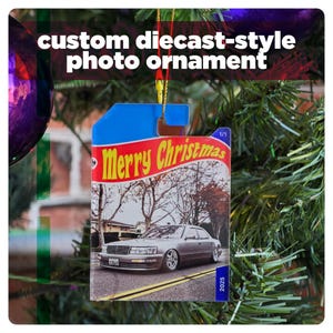 May include: A custom diecast-style photo ornament with a blue top and a picture of a silver car on a road. The ornament has the words "Merry Christmas" on a red banner. The text "2025" is visible on the bottom right.