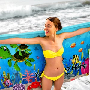 May include: A blue beach towel with a cartoon sea turtle design. The towel features a green sea turtle with a brown shell, surrounded by colorful fish and coral. The text "Your Name Here" is printed on the towel.
