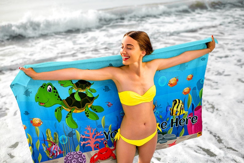 May include: A blue beach towel with a cartoon sea turtle design. The towel features a green sea turtle with a brown shell, surrounded by colorful fish and coral. The text "Your Name Here" is printed on the towel.