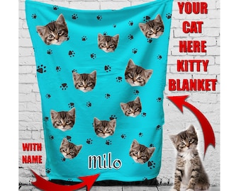 May include: A turquoise blue fleece blanket with a repeating pattern of black paw prints and a cat's face. The blanket has the name "Milo" printed on it. The text "Your Cat Here Kitty Blanket" is printed on the right side of the image. A cat is standing on the bottom right corner of the image.