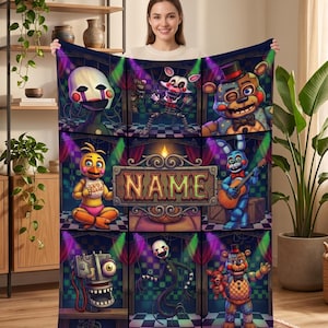 May include: A rectangular fleece blanket featuring a grid of nine panels depicting various animatronic characters from a video game series. The center panel displays a decorative sign with the word NAME in bold, stylized, orange-outlined letters.