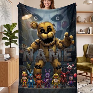 May include: A rectangular fleece blanket featuring a large, central golden bear character with dark eyes and a wide mouth. Below, a row of seven smaller colorful animatronic figures stands on a platform. The word NAME is printed in large, metallic, block letters across the center. A large, pale, masked face looms in the background under a desk lamp.