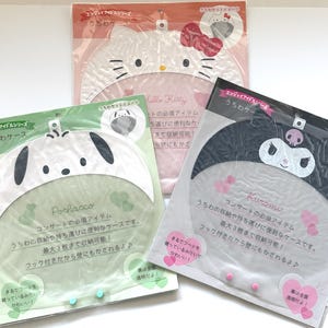 Puede incluir: Tres fundas para abanicos de personajes Sanrio en envases de plástico transparente. La funda superior presenta a Hello Kitty, la inferior izquierda a Pochacco y la inferior derecha a Kuromi. Cada funda tiene una parte superior temática.